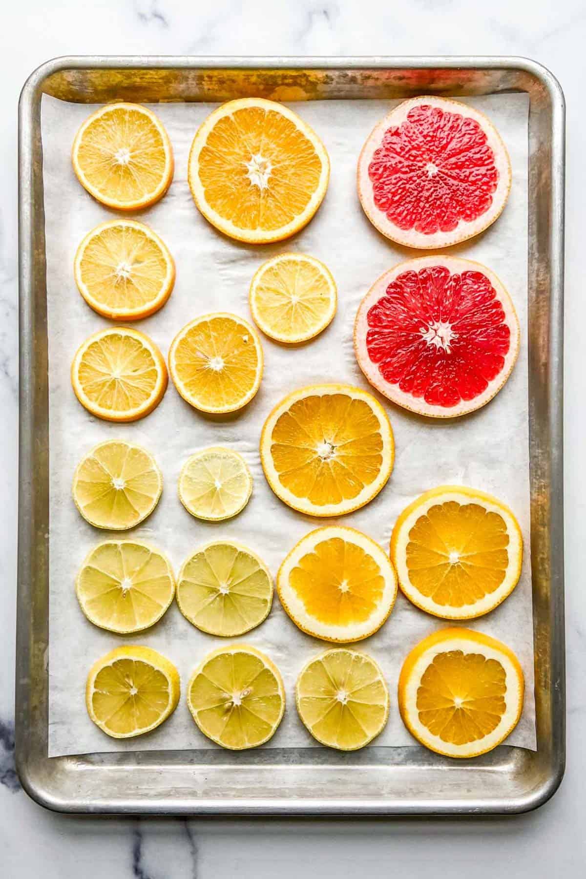 Sliced citrus fruits on a parchment lined baking sheet.