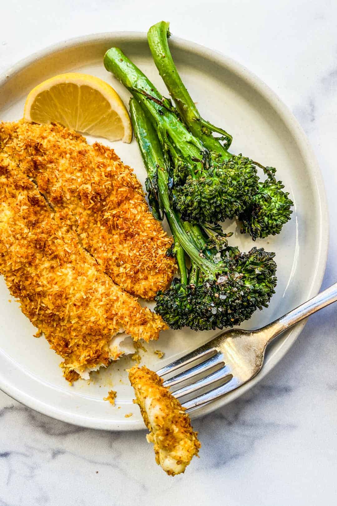 Coconut crusted tilapia next to broccolini on a white plate.