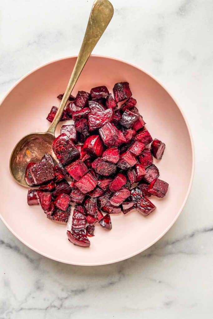 roasted beets in a pink bowl with a serving spoon
