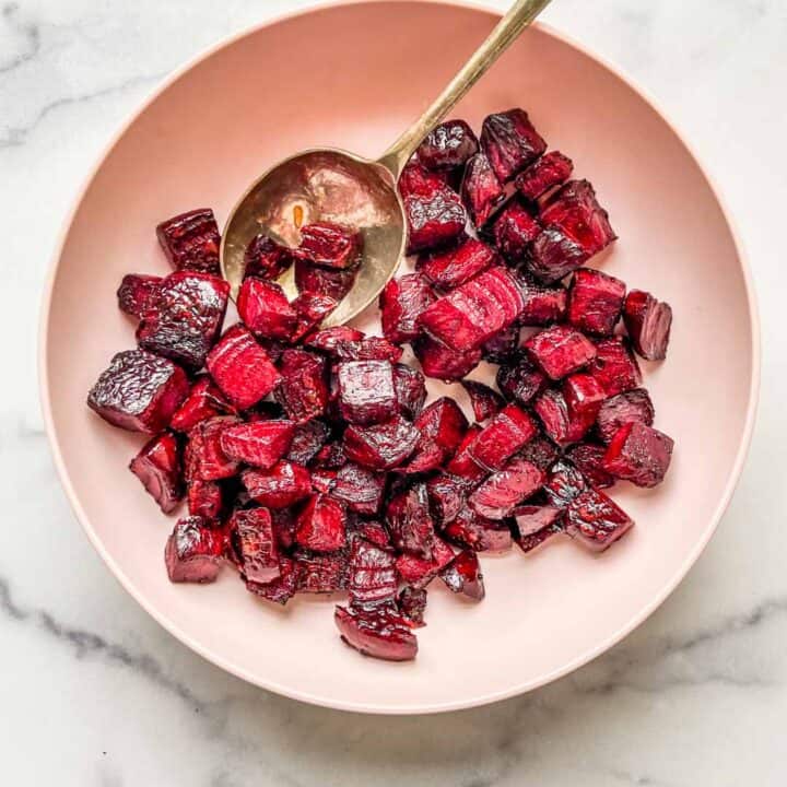 roasted beets in a pink bowl with a serving spoon