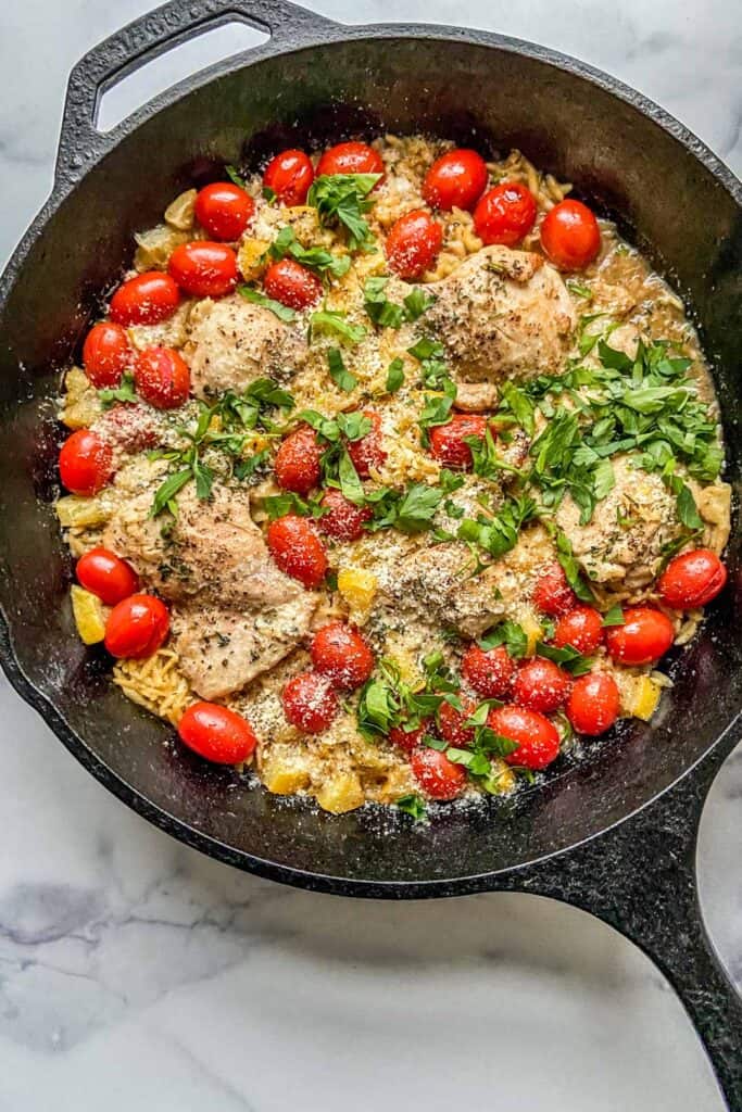 Chicken with orzo and lemons in a cast iron skillet.