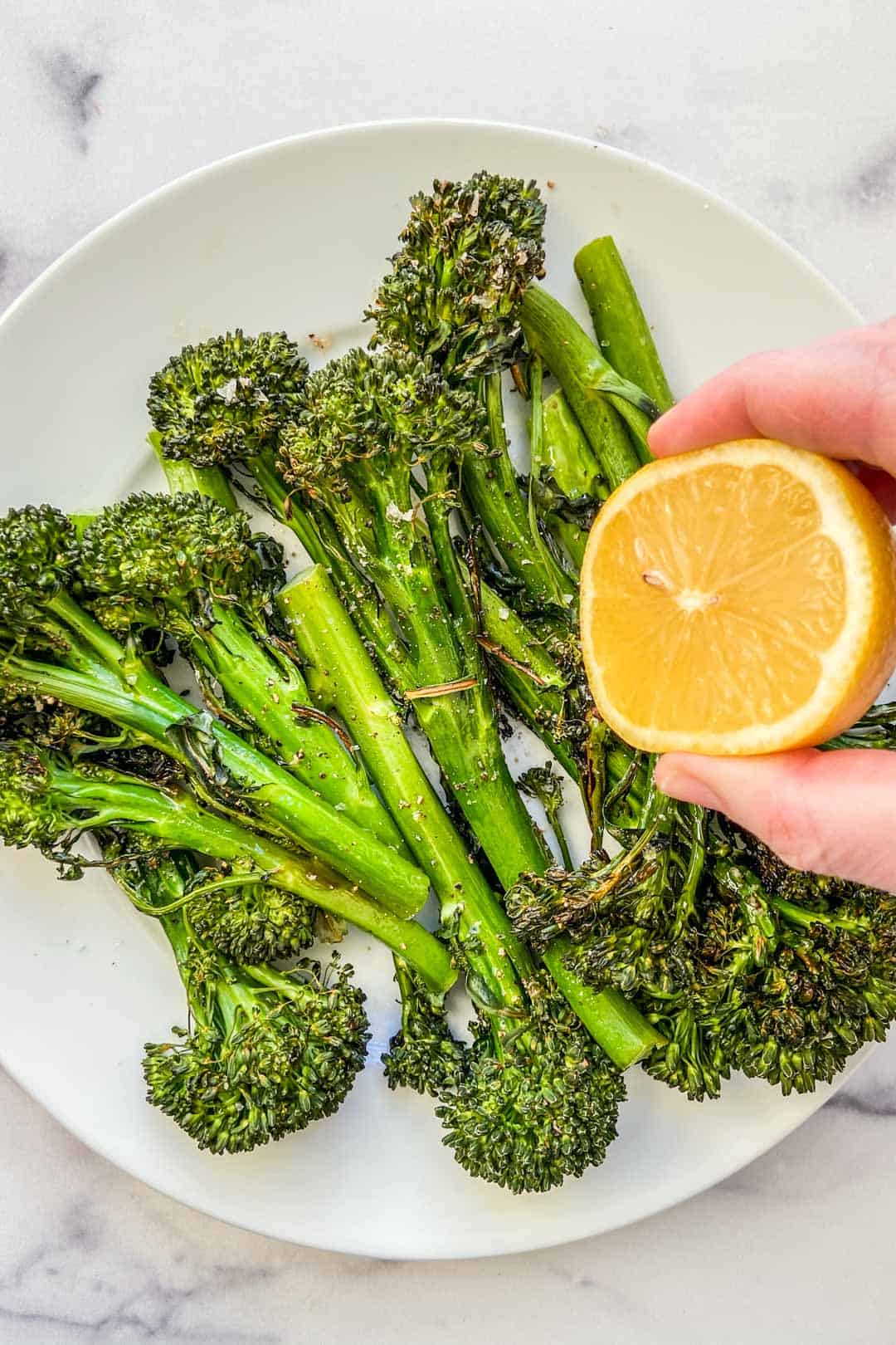 A lemon being squeezed over roasted broccolini.