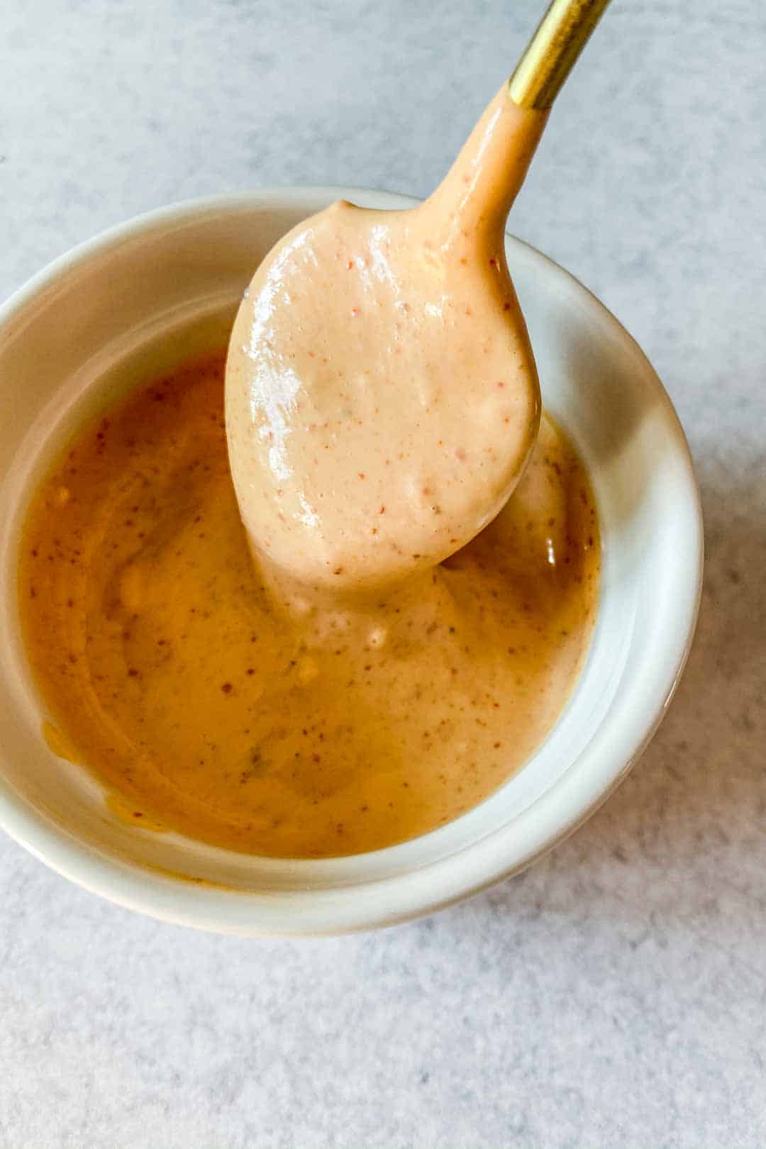 A spoon dipping into spicy mayo sauce.