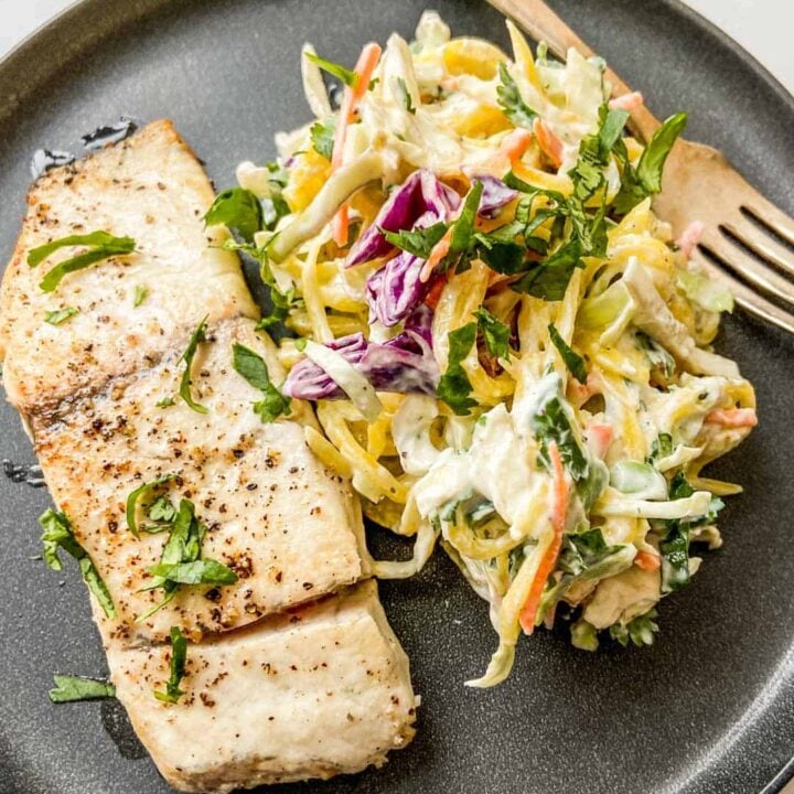 Closeup shot of a barramundi fillet next to mango slaw on a black plate with a fork.