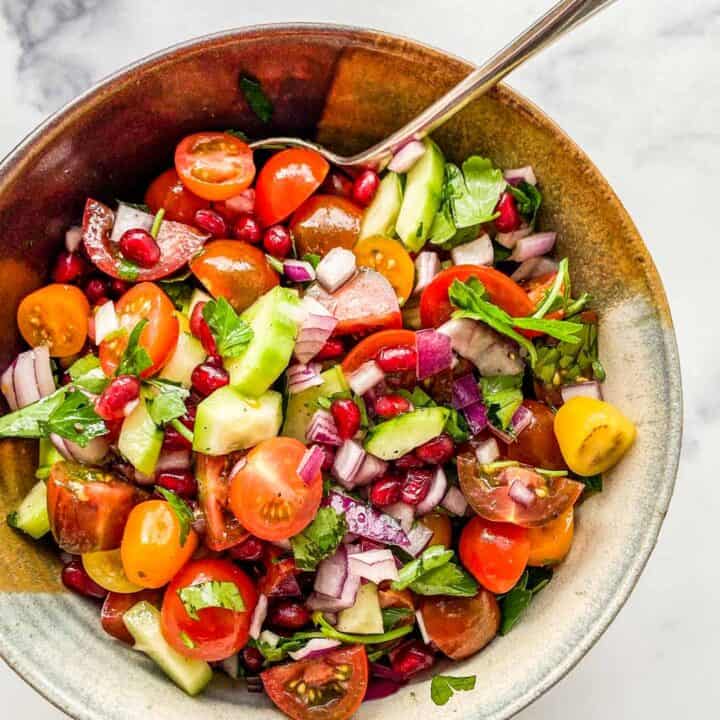 A chopped Middle Eastern salad in a ceramic bowl with a serving spoon.