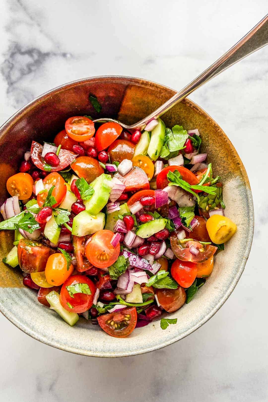 A chopped Middle Eastern salad in a ceramic bowl with a serving spoon.