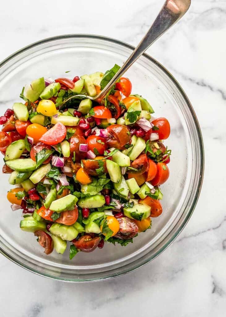 A chopped Middle Eastern salad in a mixing bowl with a serving spoon.