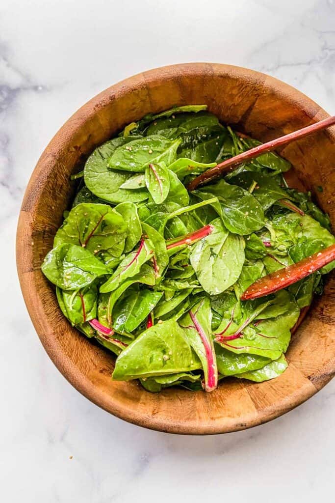 A simple green salad in a wooden bowl with wood tongs.