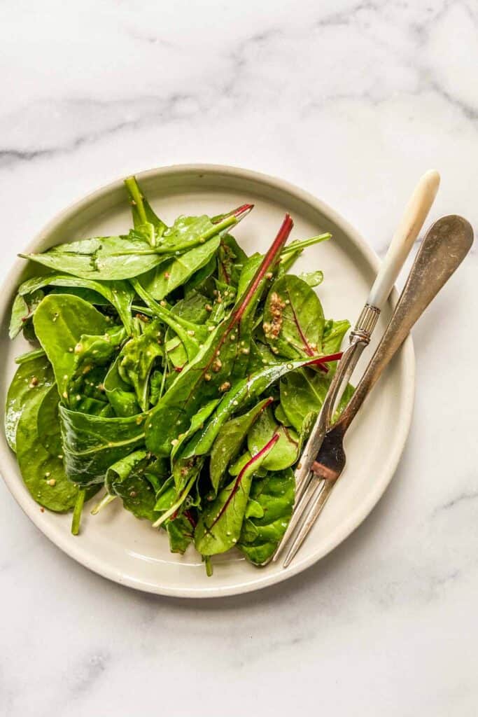 A simple green salad on a white plate with a fork and a knife.