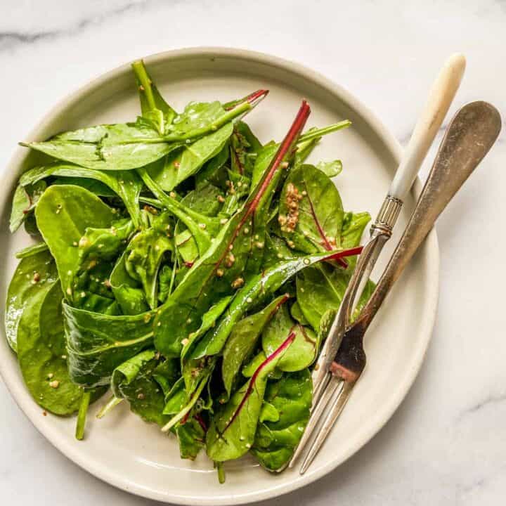 A simple green salad on a white plate with a fork and a knife.