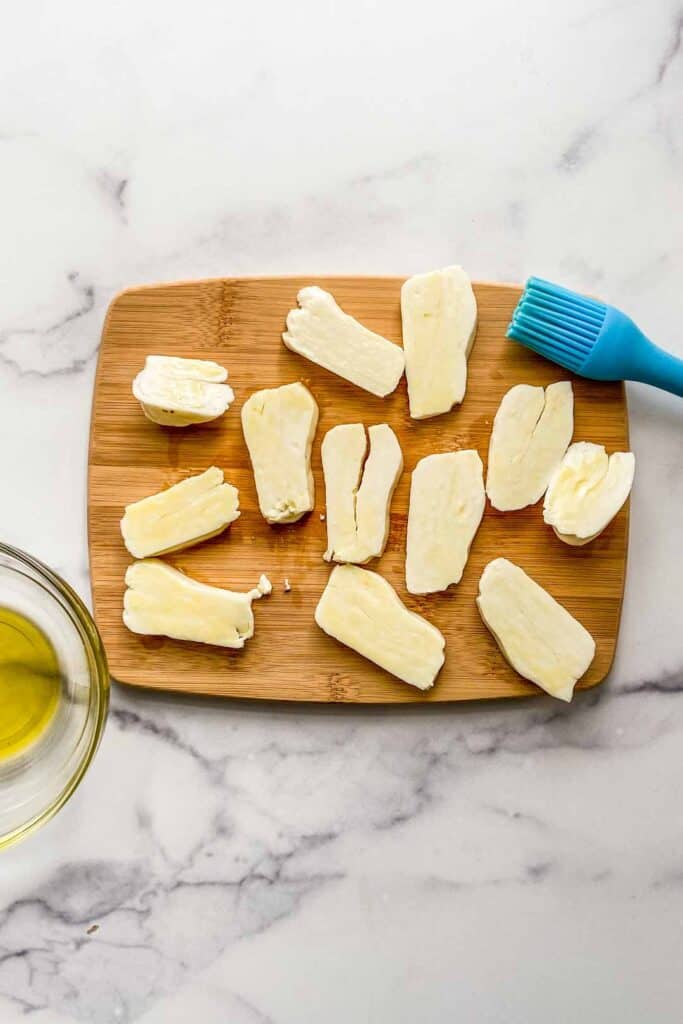 Pieces of halloumi cheese slices brushed with olive oil on a cutting board.