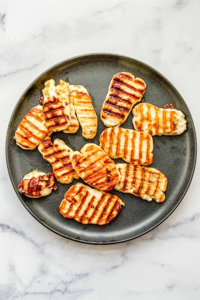 Several pieces of grilled halloumi cheese on a black plate.