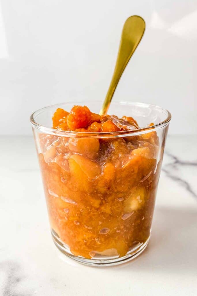 Peach compote in a glass jar with a gold spoon.