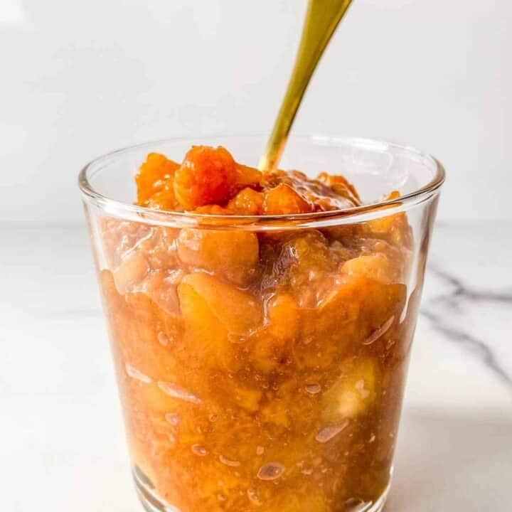 Peach compote in a glass jar with a gold spoon.