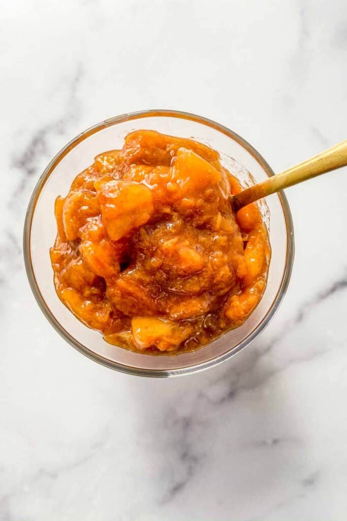 Overhead shot of a jar of peach compote with a fold spoon.