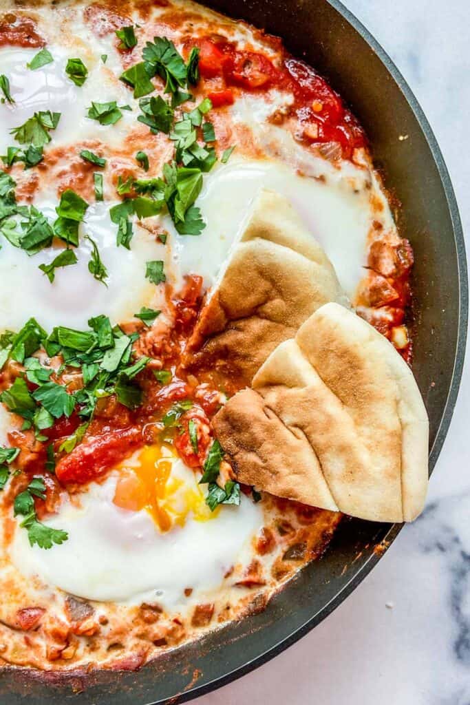 Closeup shot of shakshouka in a frying pan with two pieces of pita bread.