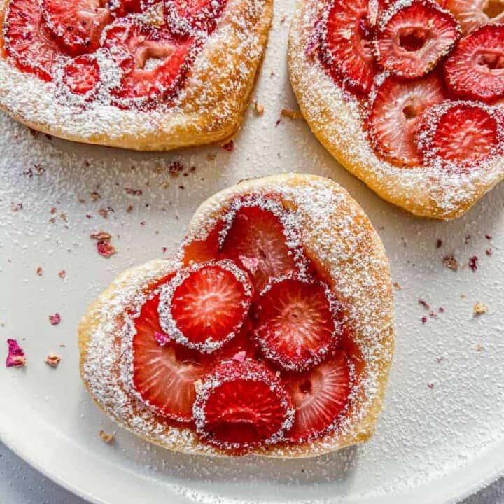 Three strawberry tartlets on a white plate.