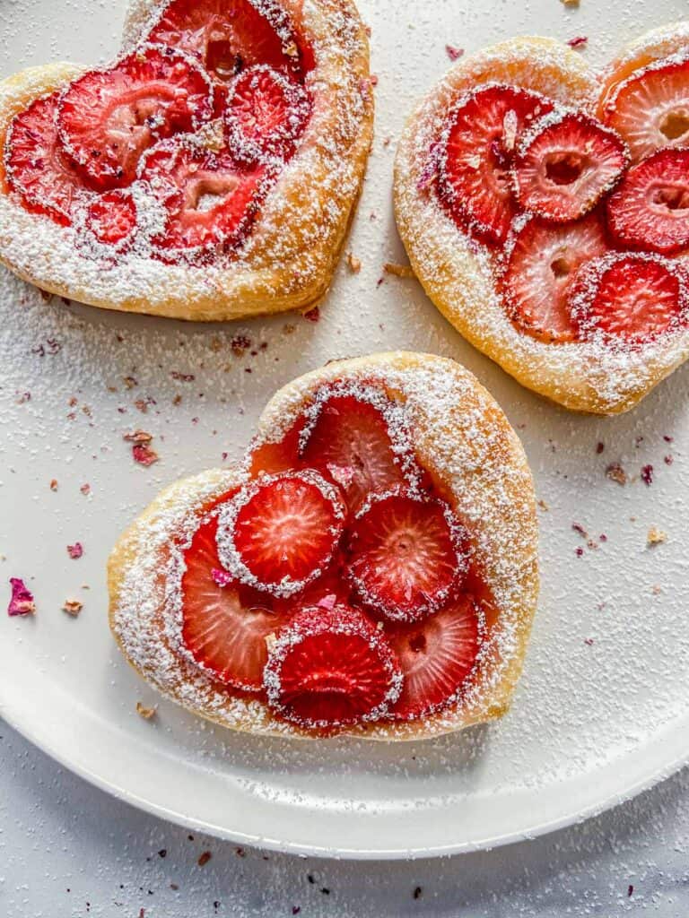 Three strawberry tartlets on a white plate.