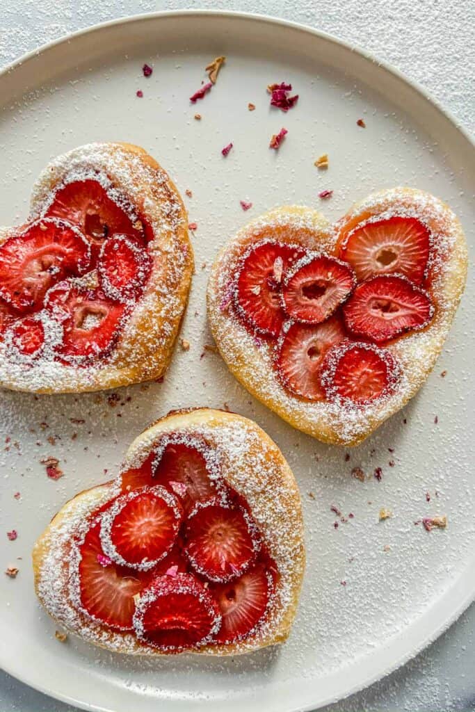 Three strawberry tarts on a white plate.