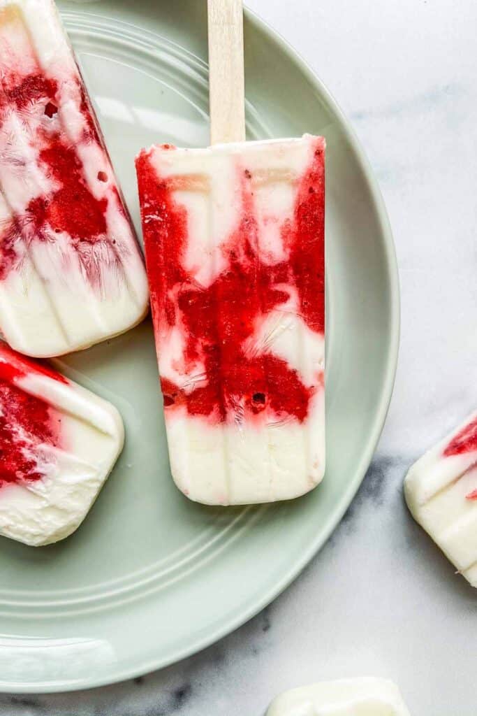 Closeup of a strawberry yogurt popsicle on a light green plate.