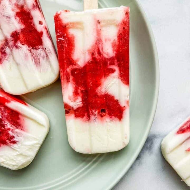 Closeup of a strawberry yogurt popsicle on a light green plate.