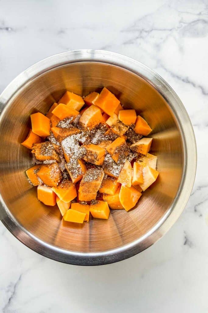 Chopped butternut squash with za'atar, olive oil, and salt in a metal bowl.