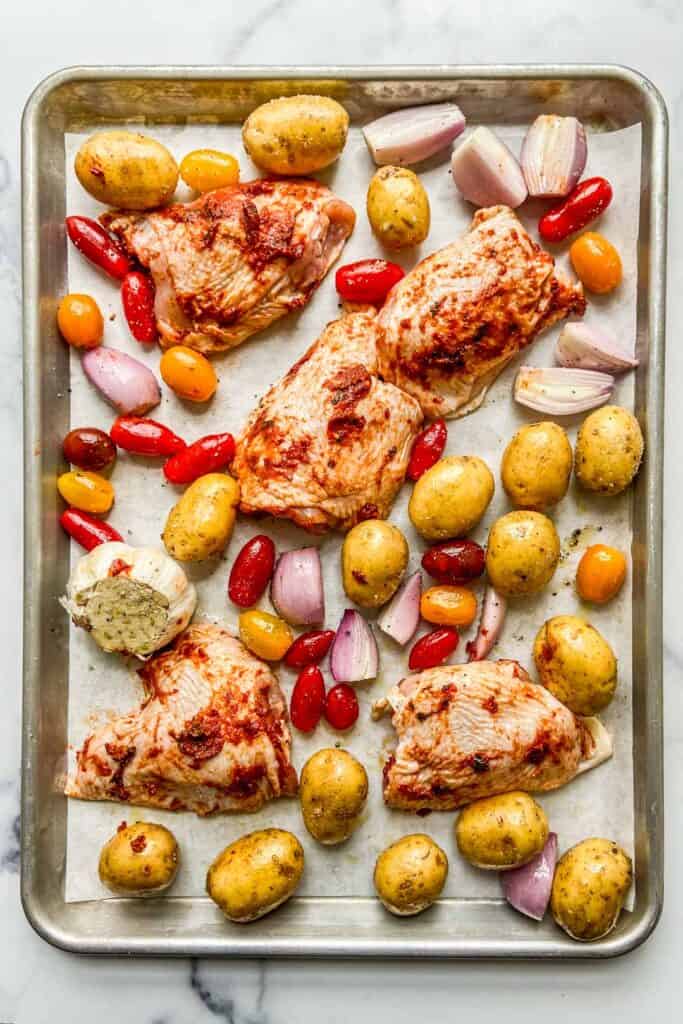 A sheet pan with uncooked chicken, potatoes, and tomatoes.