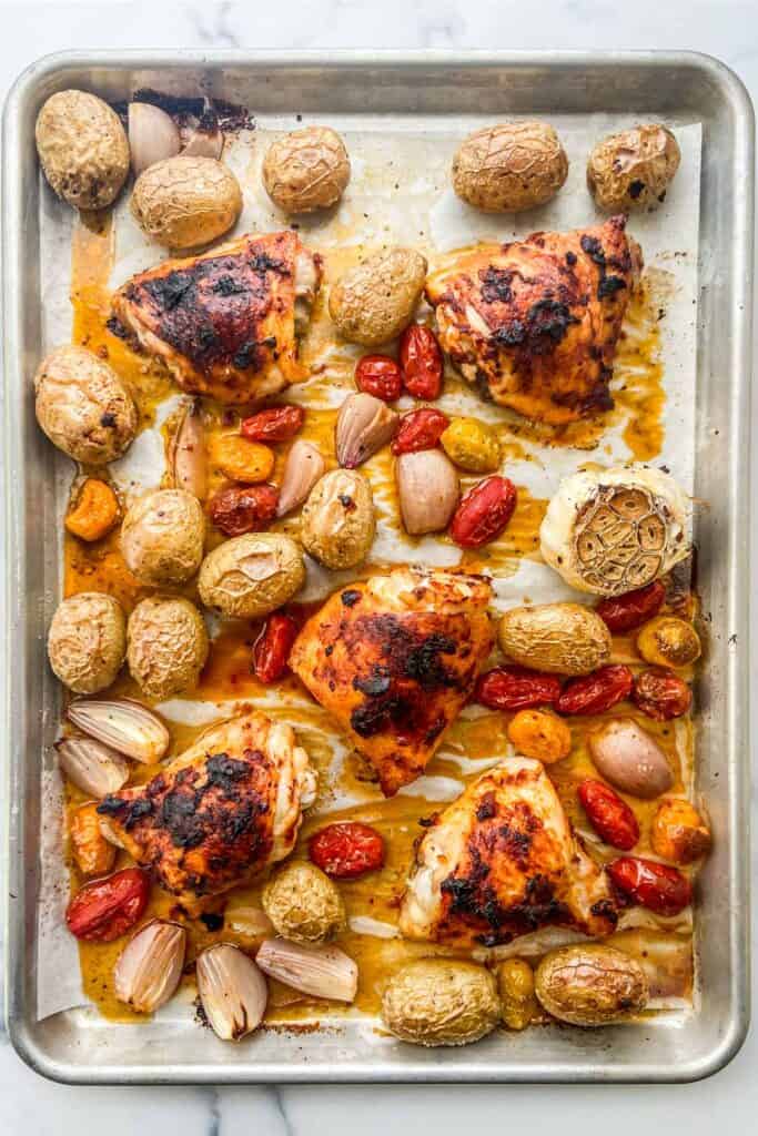 A sheet pan with roasted chicken, potatoes, tomatoes, and a head of garlic.