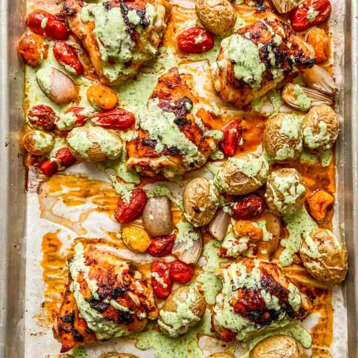 A sheet pan with roasted chicken, potatoes, tomatoes, and drizzled with a garlic yogurt sauce.