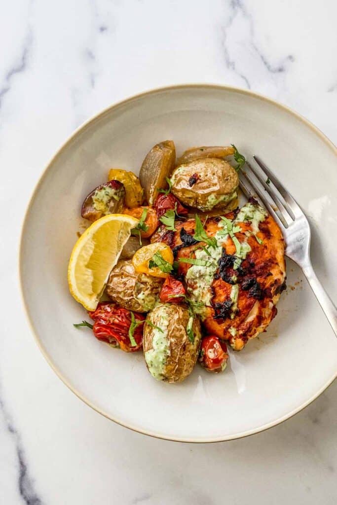 A bowl of harissa chicken with potatoes and tomatoes.