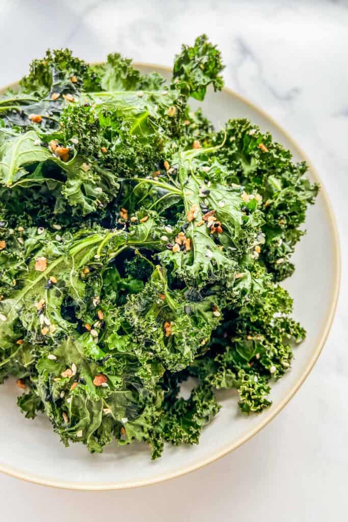 A bowl of kale chips sitting on a marble background.