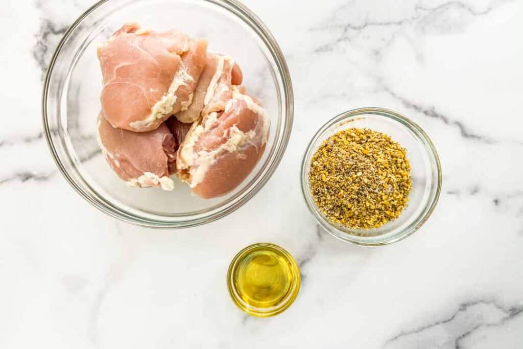 Ingredients for lemon pepper chicken on a marble background.
