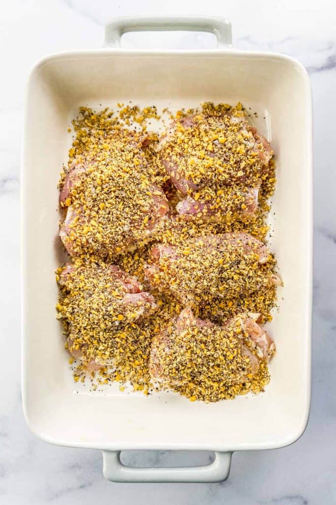 Chicken thighs in a baking dish topped with lemon pepper seasoning.