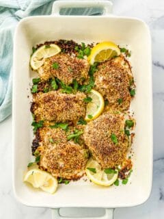 A baking dish with chicken thighs covered in lemon pepper seasoning.