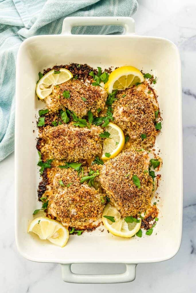 A baking dish with chicken thighs covered in lemon pepper seasoning.