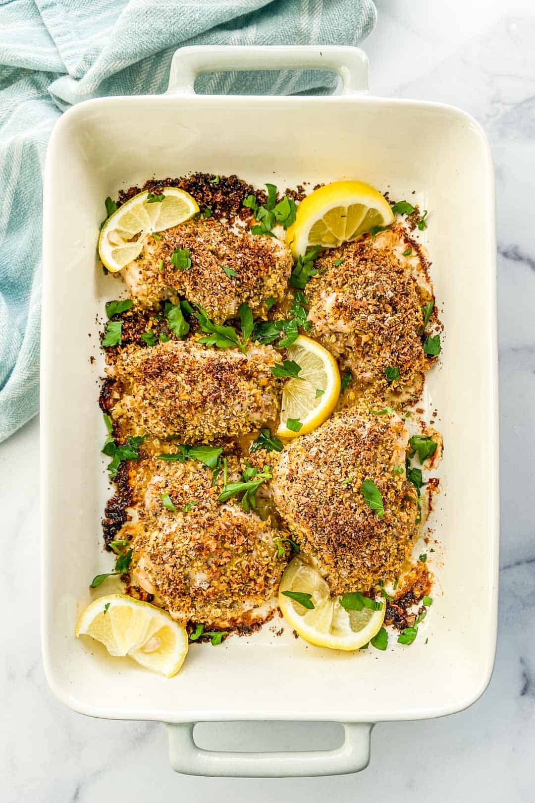 A baking dish with chicken thighs covered in lemon pepper seasoning.