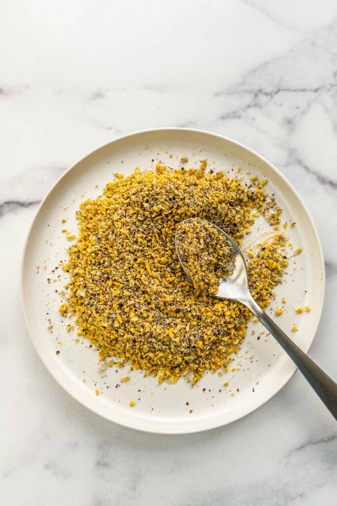 An overhead shot of a plate of lemon pepper seasoning with a spoon.