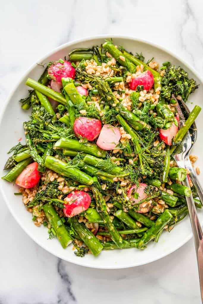 A large white serving bowl of farro and vegetable salad with a silver spoon.