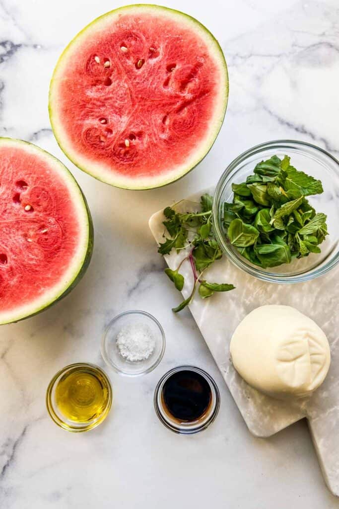 Ingredients for a watermelon mozzarella salad on a marble background.