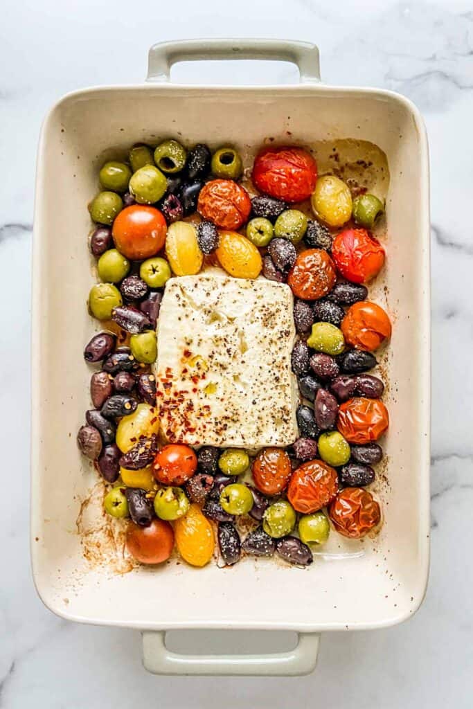 A baking dish with a block of feta, olives, and tomatoes.