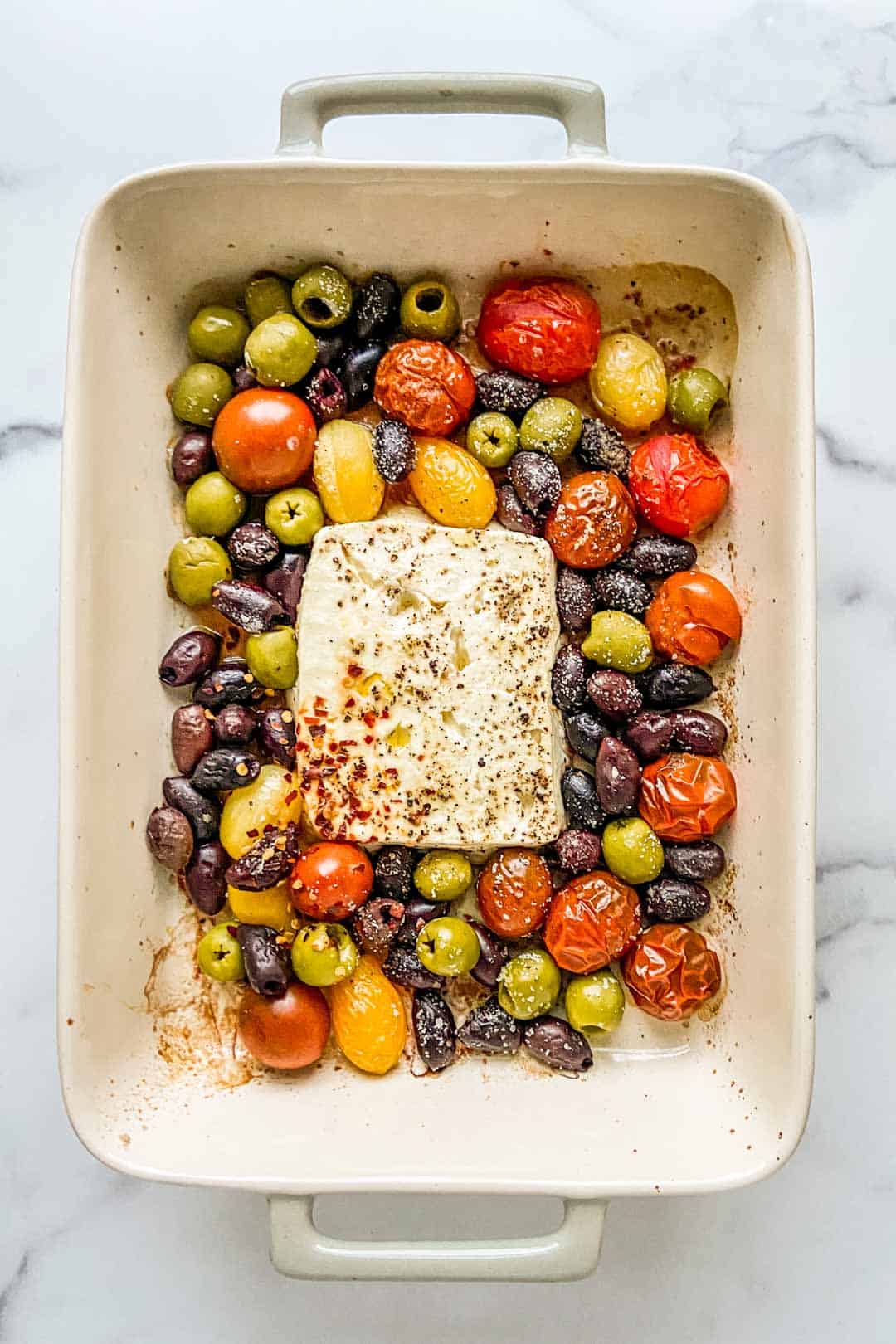 A baking dish with a block of feta, olives, and tomatoes.