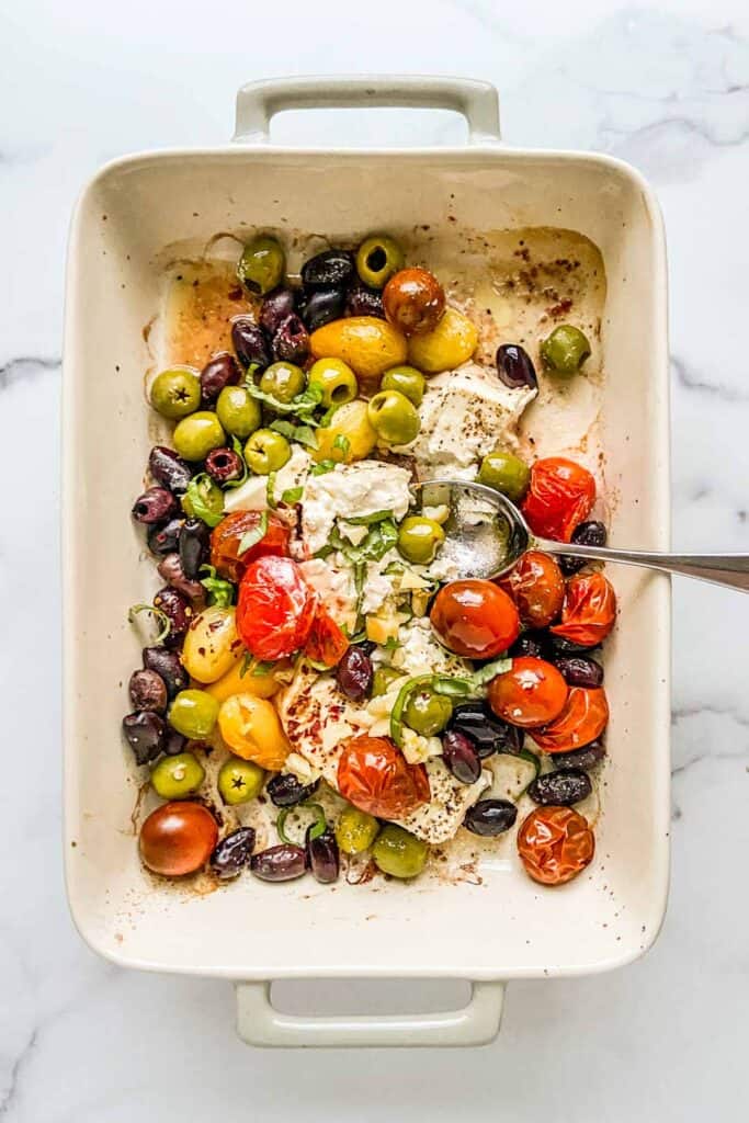 An overhead shot of a baking dish with feta, olives, and tomatoes.