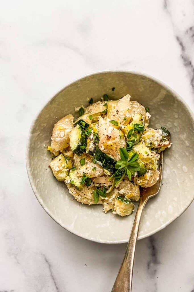 A bowl of baked feta and zucchini pasta with a silver spoon.