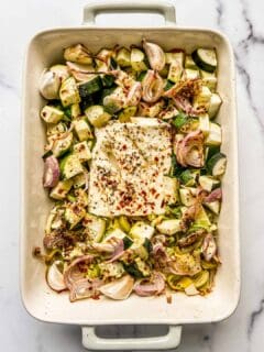 An overhead shot of a baking dish with feta, zucchini, leeks, and shallots.