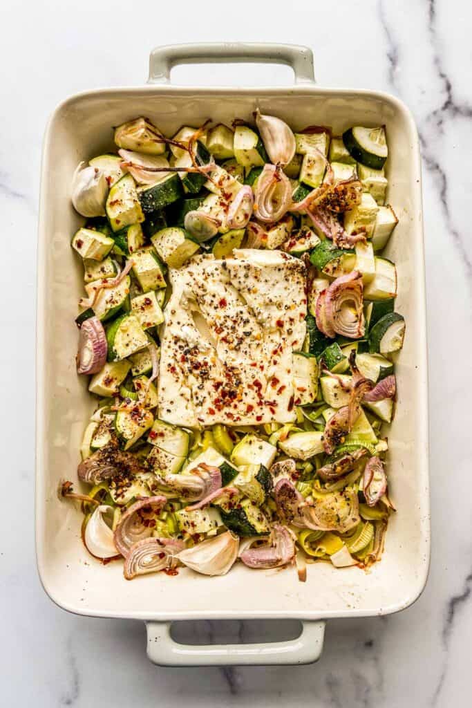 An overhead shot of a baking dish with feta, zucchini, leeks, and shallots.