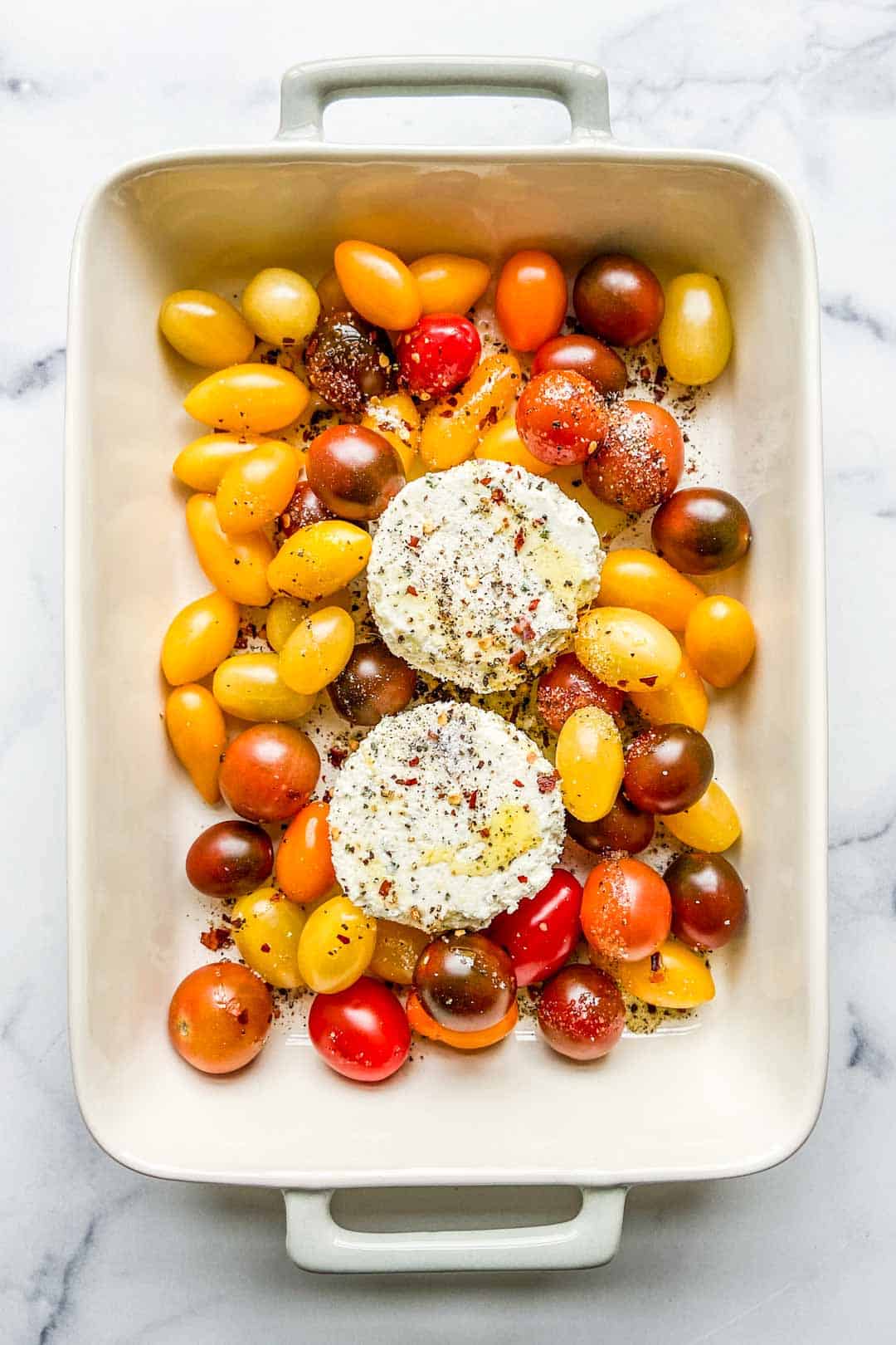 A baking dish with two Boursin pieces and cherry tomatoes.