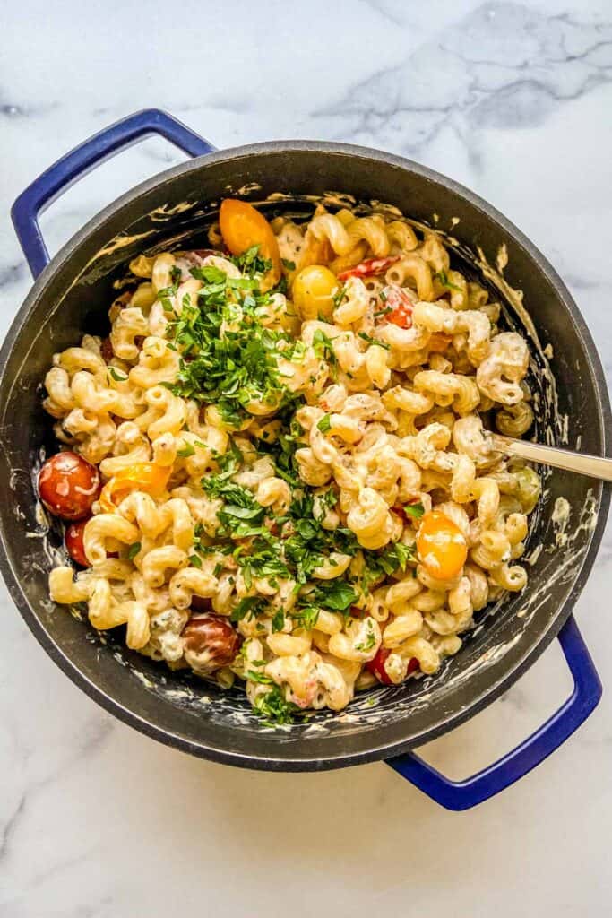 A blue dutch oven with pasta topped with herbs.