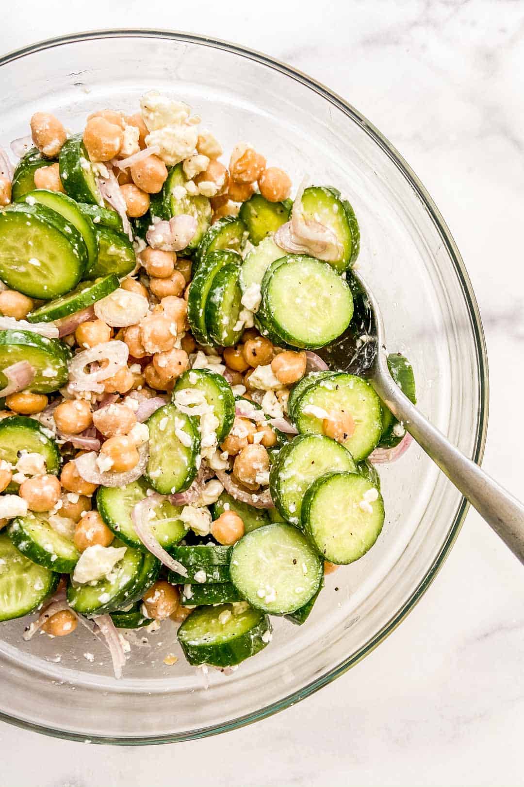 A closeup shot of a bowl of cucumber chickpea salad with a silver spoon.
