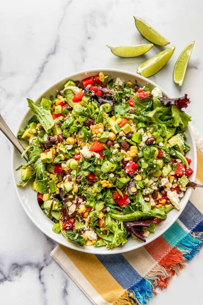 A bowl of grilled corn and bean salad on a colorful napkin with a few slices of cut lime.