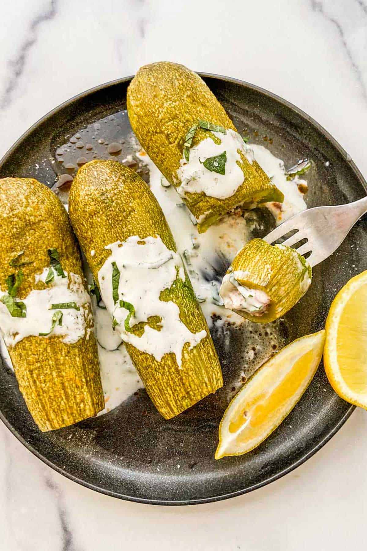 Stuffed kousa with a yogurt sauce on a black plate.